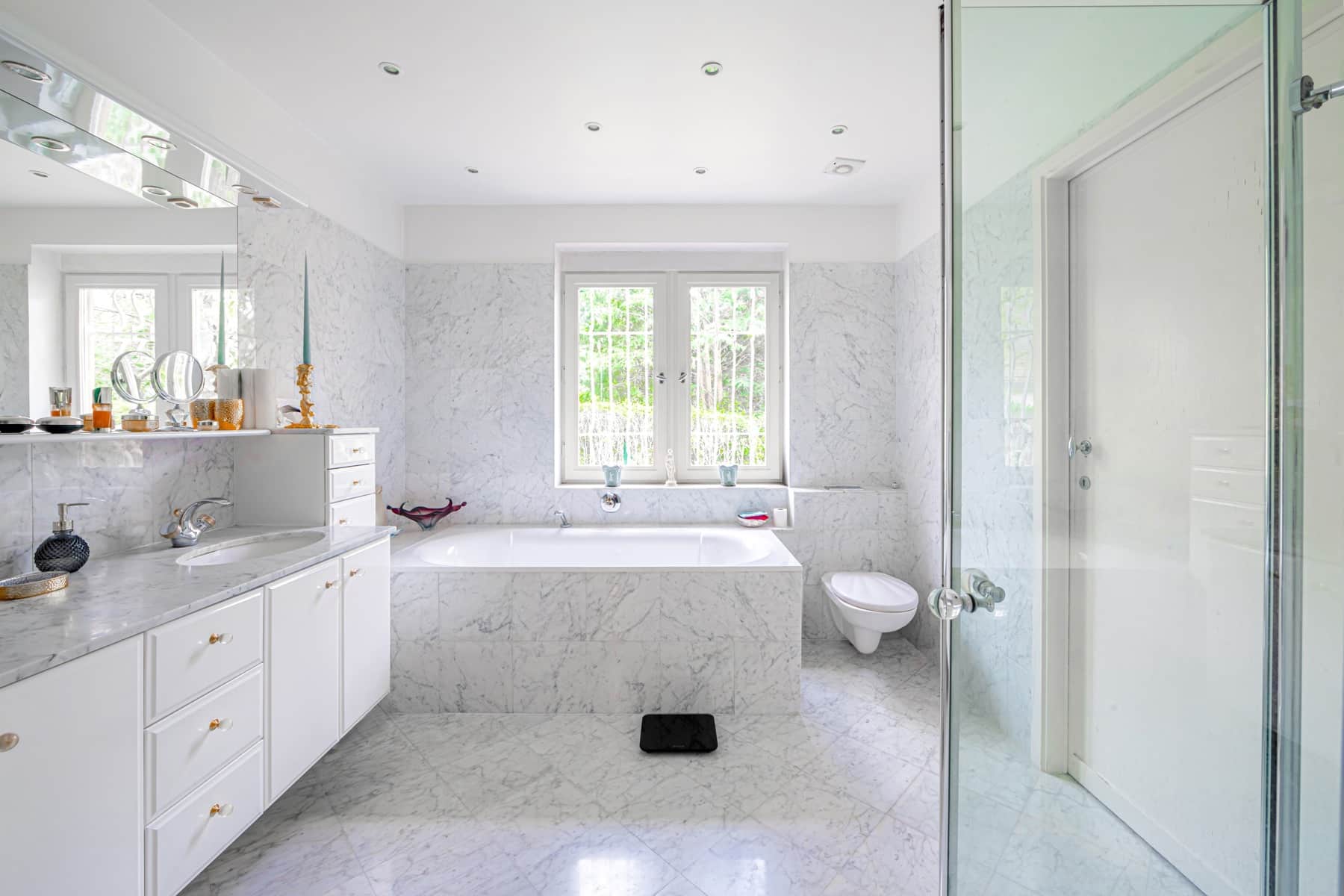 Salle de bain contemporaine en marbre blanc, baignoire design et vue verdoyante.