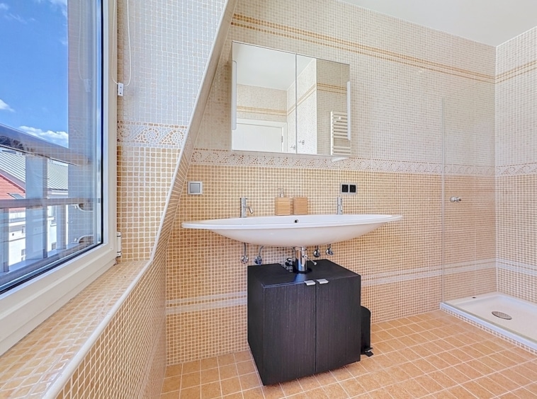 Salle de bain moderne avec mosaïque claire, lavabo mural, éclairage naturel, design épuré et élégant.