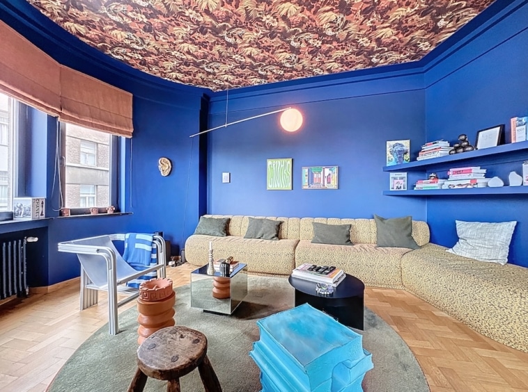 Salon éclectique en bleu vif avec mobilier moderne, coussins verts et décoration artistique.