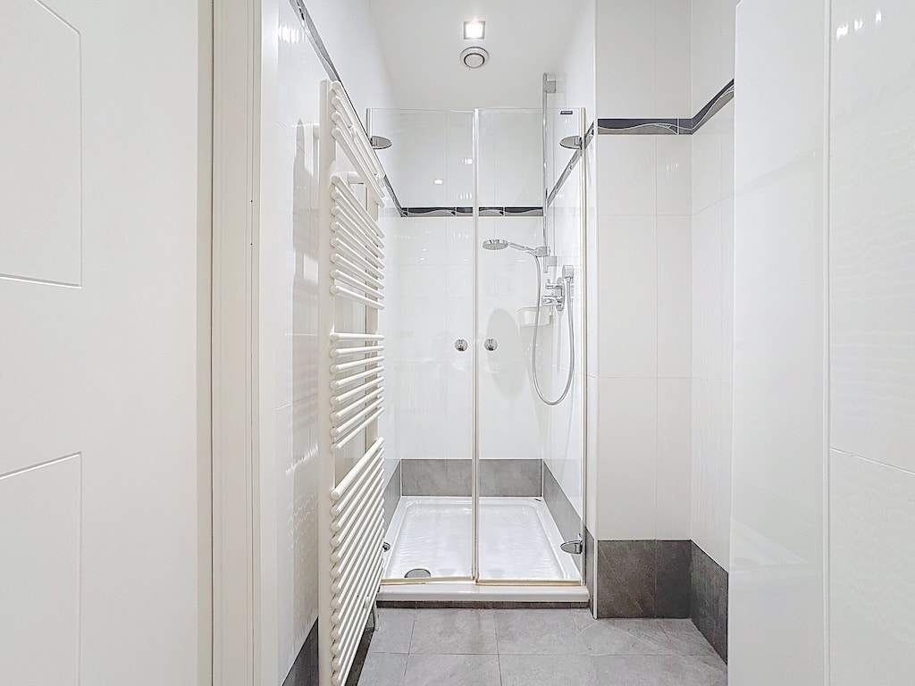 Salle de douche moderne en verre, murs blancs, sol gris foncé, radiateur blanc, design épuré.