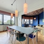 Salle à manger moderne avec table colorée, éclairage doux et espace cosy au mur bleu vif.