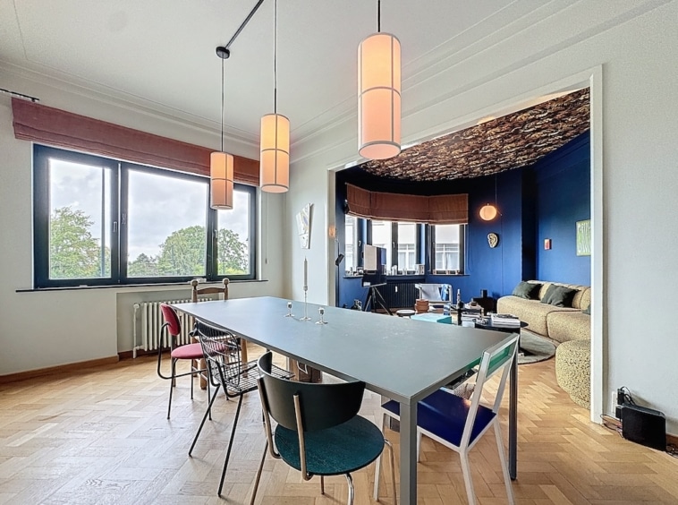 Salle à manger moderne avec table colorée, éclairage doux et espace cosy au mur bleu vif.