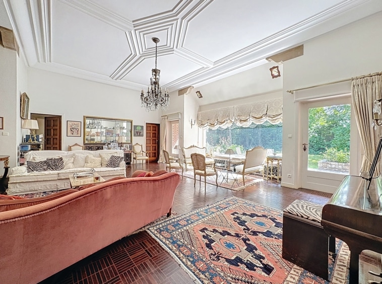 Salon lumineux et élégant avec piano, mobilier raffiné et vue verdoyante extérieure.