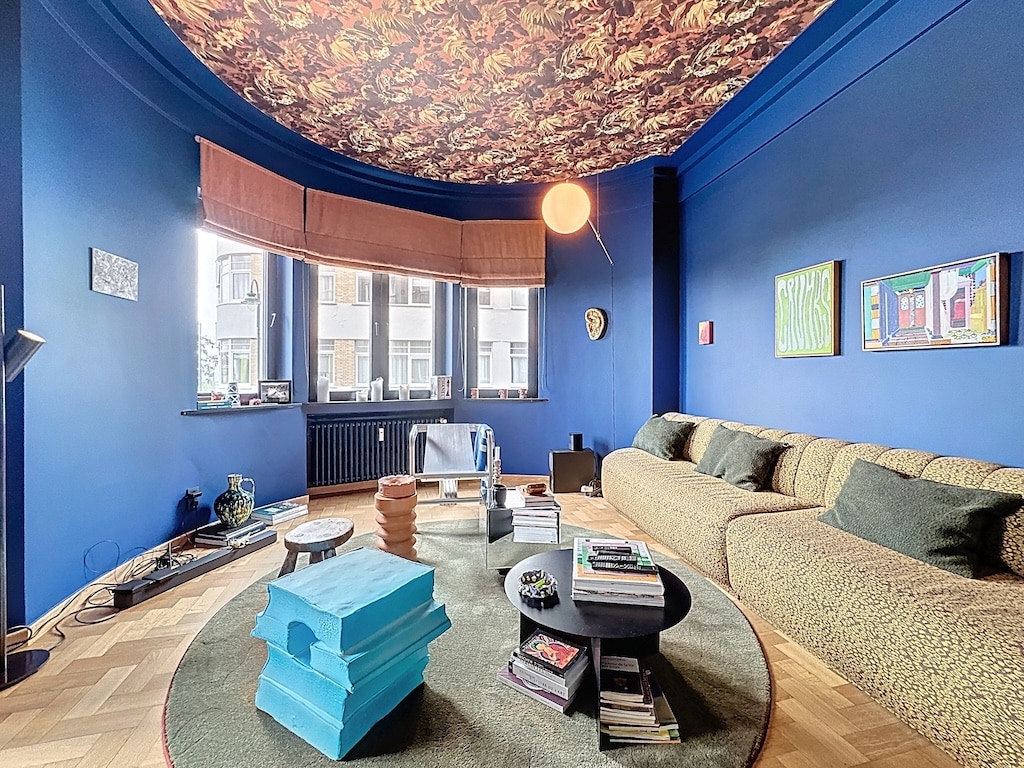 Salon moderne avec murs bleus, plafond floral, canapé cosy et décoration artistique colorée.