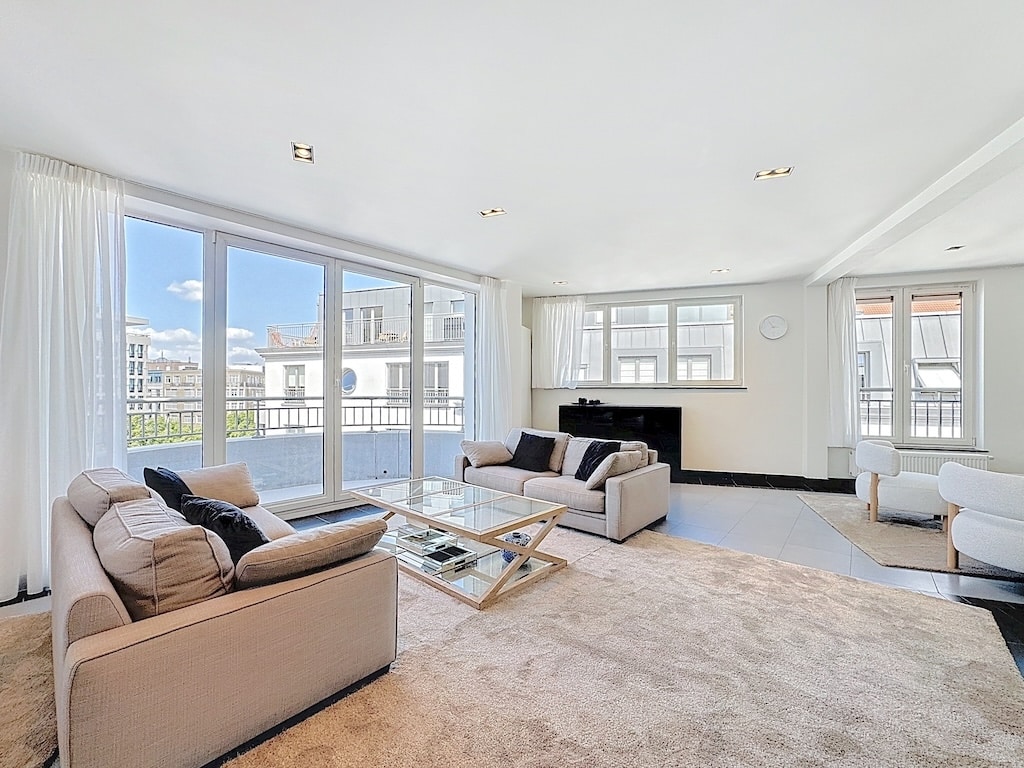 Salon moderne lumineux avec vue urbaine, canapé clair, cheminée élégante, ambiance chic et chaleureuse.