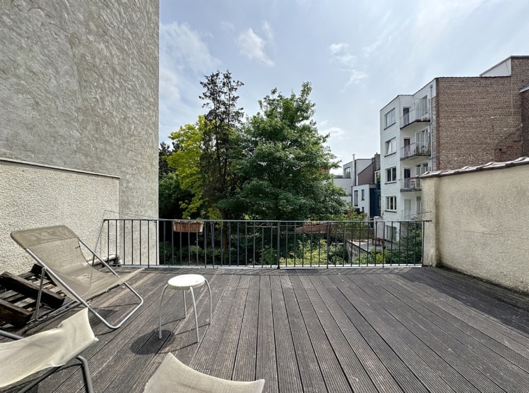 Terrasse urbaine avec mobilier lounge, vue verdoyante et architecture variée sous ciel partiellement nuageux.