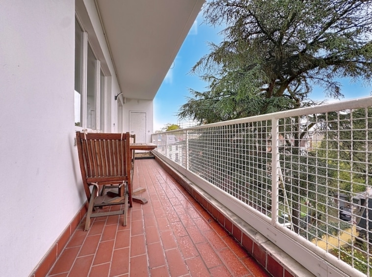 Balcon lumineux avec mobilier en bois, vue sur un arbre vert et ciel bleu paisible.