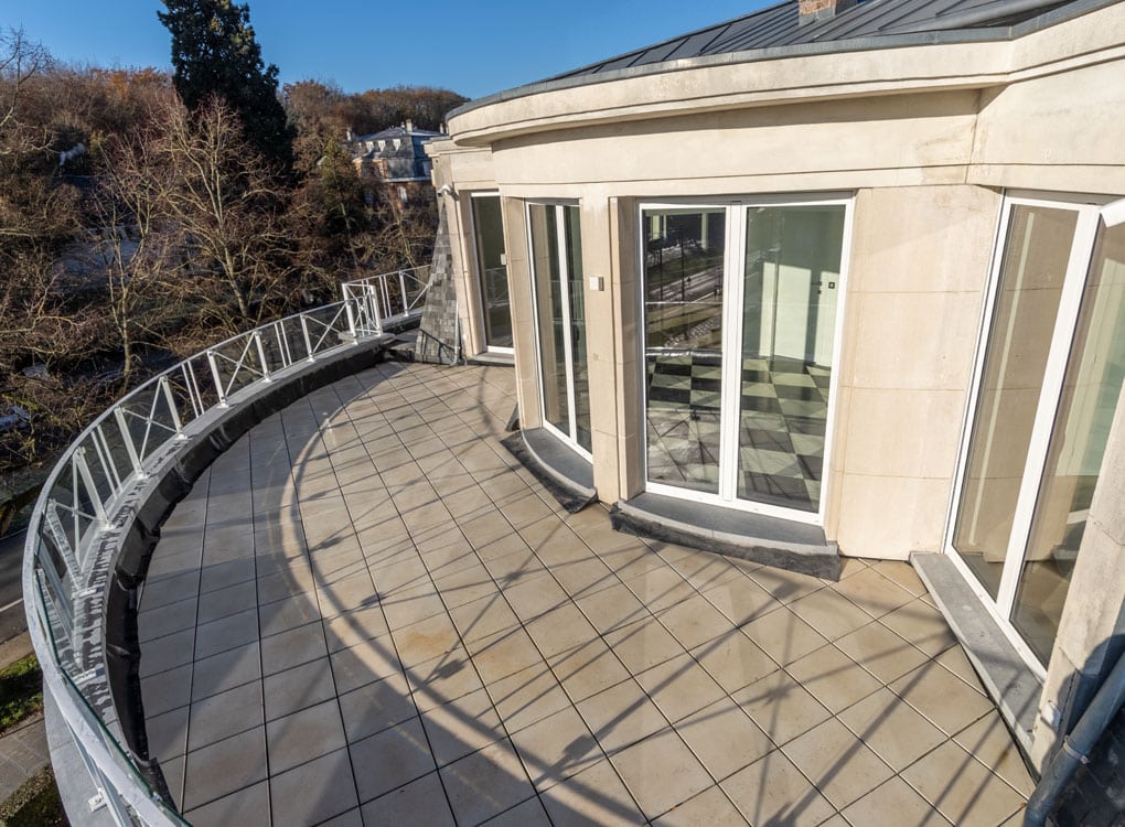 Balcon courbé moderne avec vue panoramique, verre, bois et verdure, idéal pour détente et apéritifs.