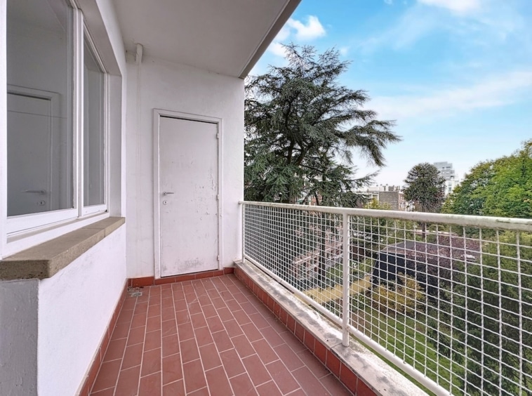 Balcon lumineux avec vue sur nature, sol en carreaux rouges, murs blancs et espace de détente urbain.