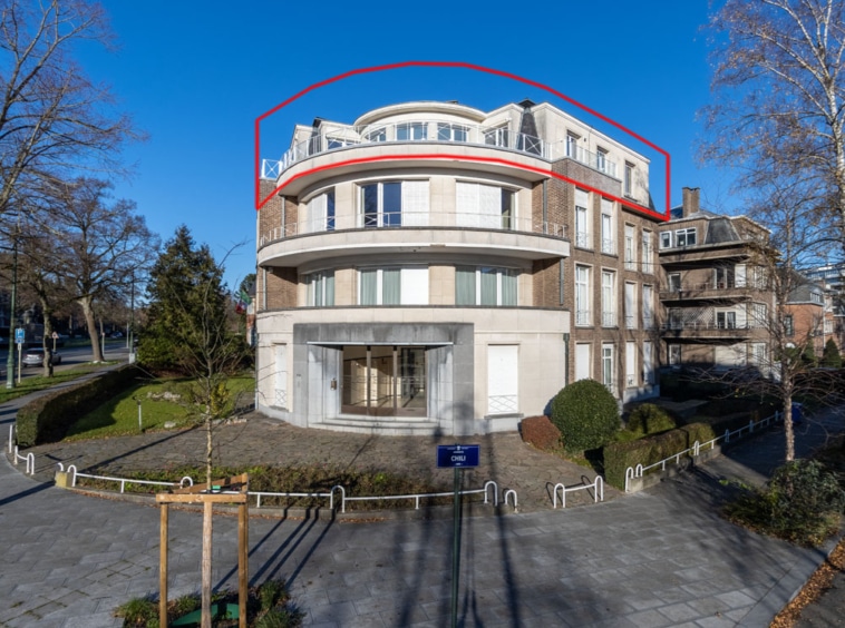 Bâtiment moderne avec façade en pierre, grandes fenêtres, terrasse sur le toit et jardin soigné.