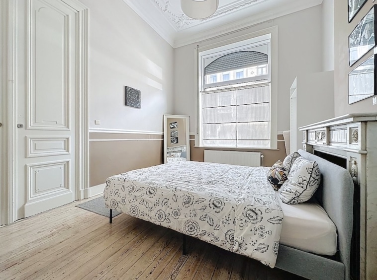 Chambre lumineuse et élégante avec lit floral, miroir, mobilier minimaliste et ambiance zen.
