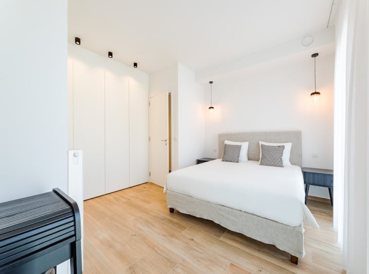 Chambre moderne minimaliste lumineuse avec lit blanc, éclairage doux et rangements épurés.