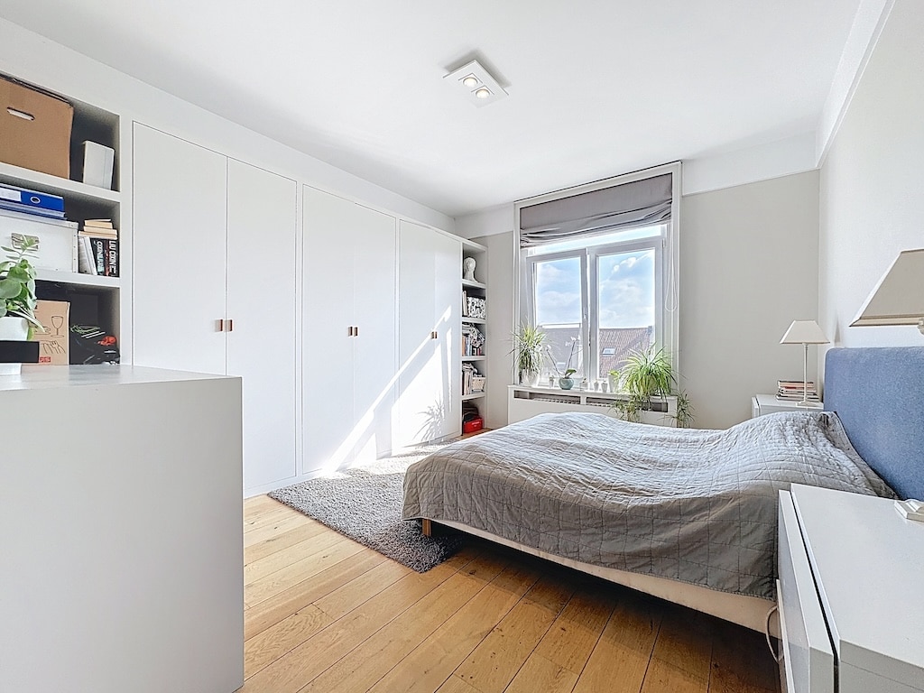Chambre moderne minimaliste lumineuse avec lit gris, mobilier épuré et touches de verdure.