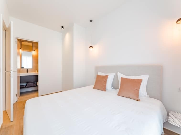 Chambre moderne, lumineuse, apaisante avec lit blanc, éclairage doux et accès à salle de bain élégante.
