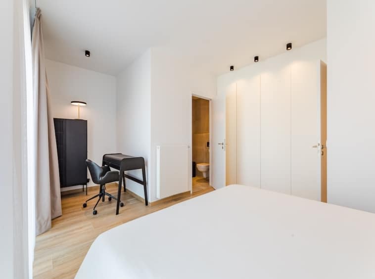 Chambre moderne lumineuse avec grand lit, espace de travail, salle de bain attenante, design épuré.