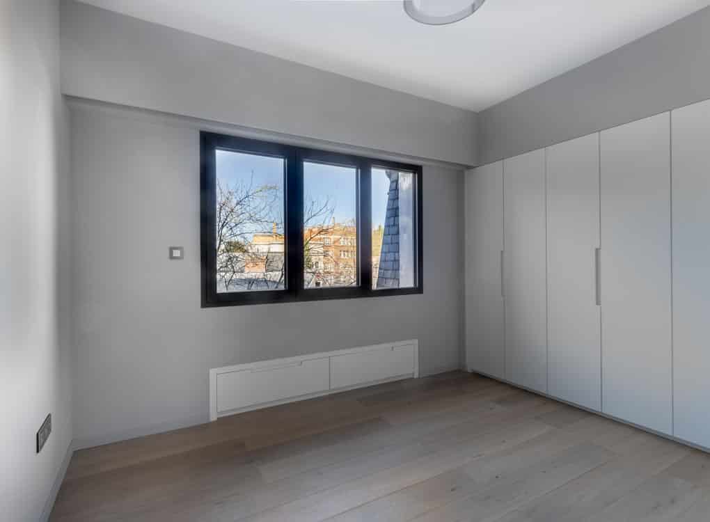 Chambre contemporaine minimaliste avec lumière naturelle, murs gris, mobilier blanc épuré et parquet clair.