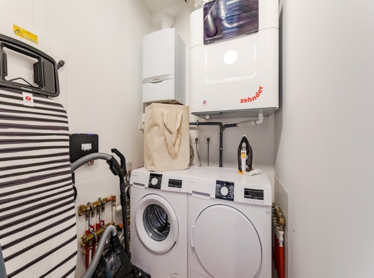 Coin buanderie compacte, lave-linge empilé, sèche-linge, planche à repasser à rayures, espace organisé.
