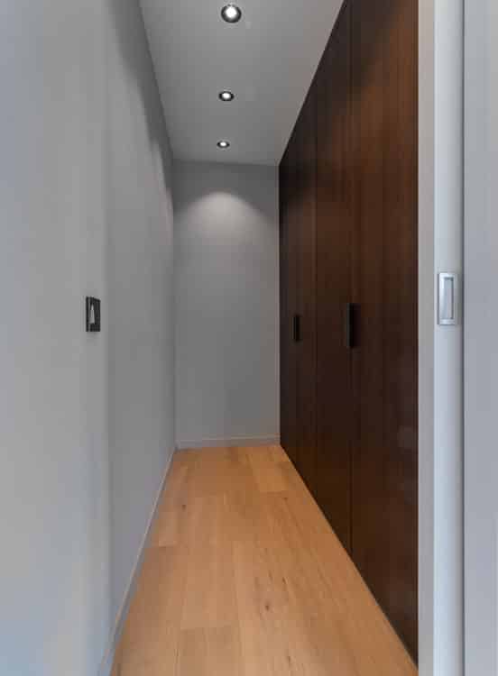 Couloir moderne en bois clair, panneau en bois foncé, éclairage doux, ambiance calme et élégante.