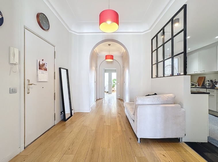Couloir moderne lumineux avec salon blanc, arc design, lampe rouge et cuisine ouverte translucide.