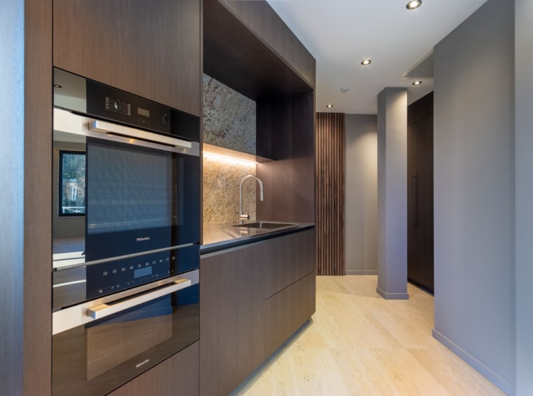 Cuisine moderne en bois foncé avec appareils intégrés, éclairage naturel, ambiance élégante et fonctionnelle.