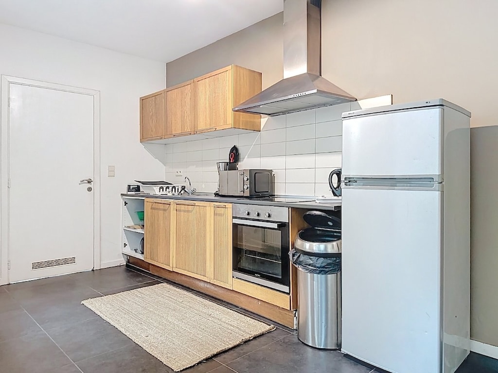 Cuisine moderne et lumineuse avec mobilier en bois clair, électroménagers inox et sol foncé élégant.