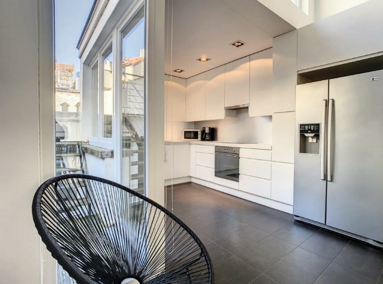 Cuisine moderne lumineuse avec appareils en inox, mobilier blanc et fauteuil design.