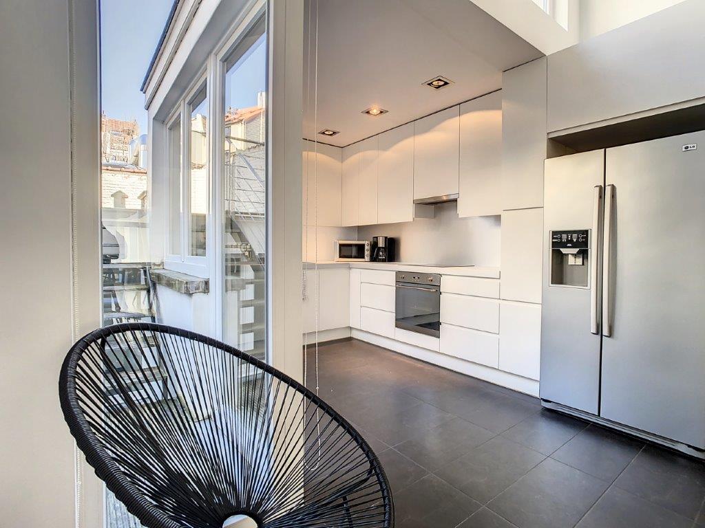 Cuisine moderne lumineuse avec appareils en inox, mobilier blanc et fauteuil design.
