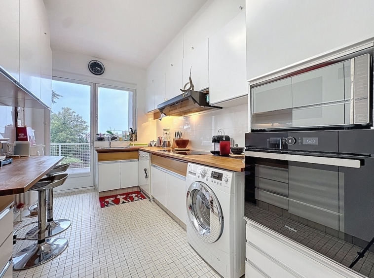 Cuisine moderne lumineuse avec rangement blanc, plan en bois, coin repas et appareils élégants.