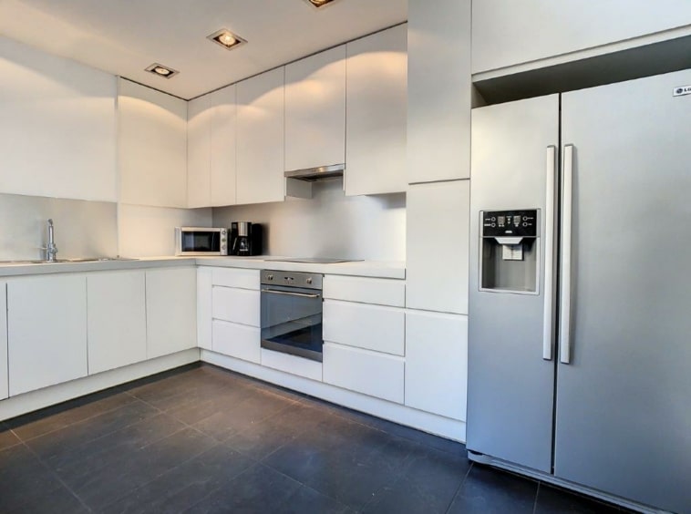 Cuisine moderne minimaliste avec électroménagers encastrés, surfaces blanches et éclairage intégré.