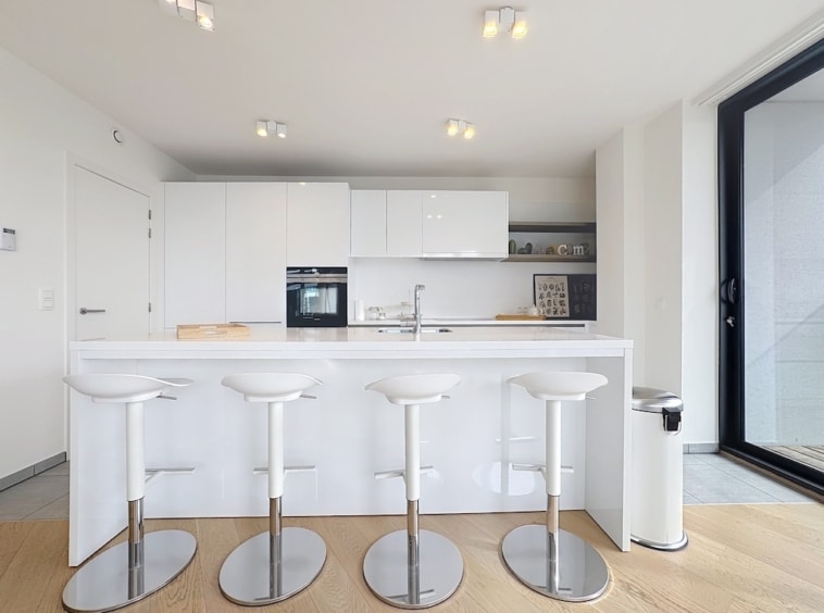 Cuisine moderne minimaliste avec îlot central blanc, appareils encastrés et éclairage naturel.