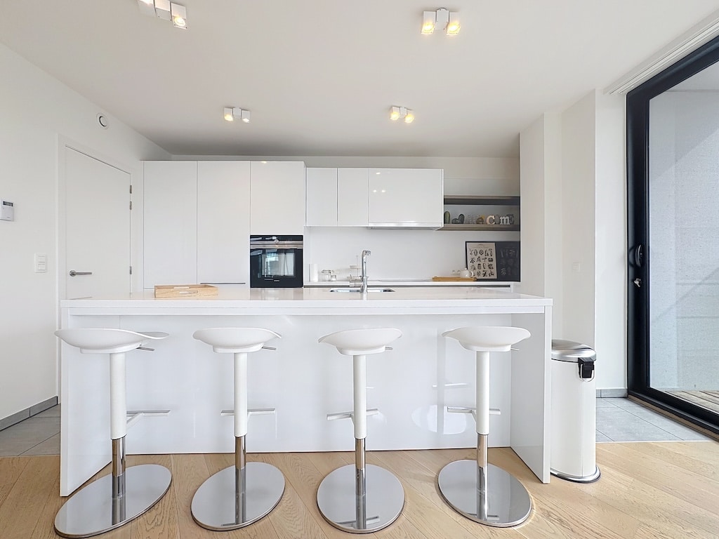 Cuisine moderne minimaliste avec îlot central blanc, appareils encastrés et éclairage naturel.
