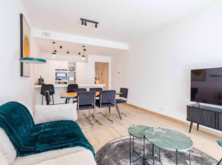 Salon moderne minimaliste avec canapé beige, mobilier épuré, espace dining élégant et lumière chaleureuse.