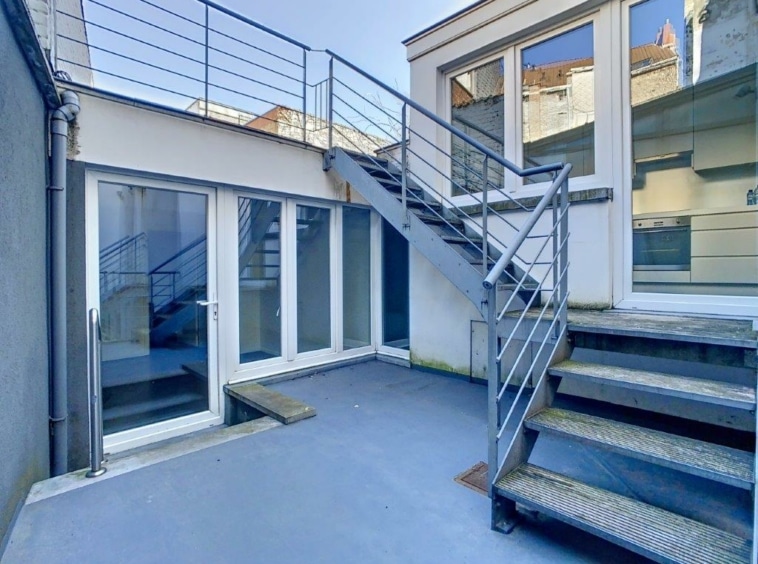 Esprit moderne avec escalier en béton, portes en verre et terrasse lumineuse extérieure.