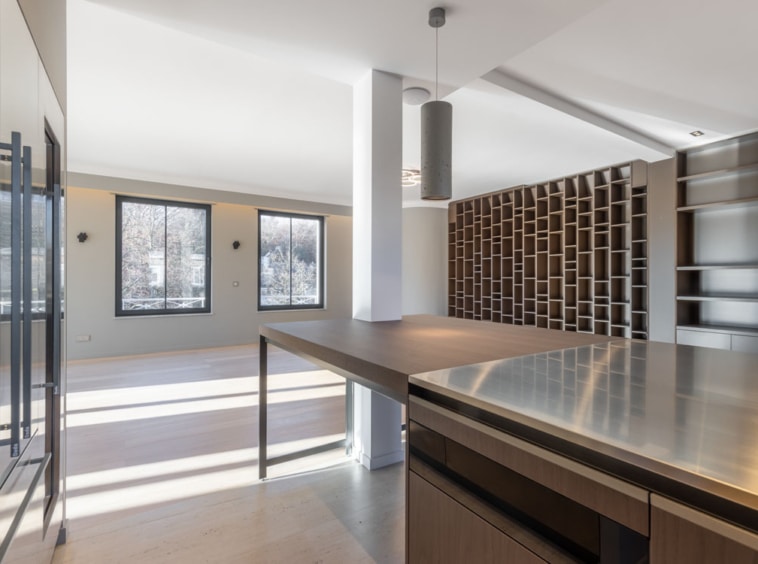 Espace moderne cuisine ouverte, lumineux, avec îlot en acier, étagère design en bois et vue extérieure.