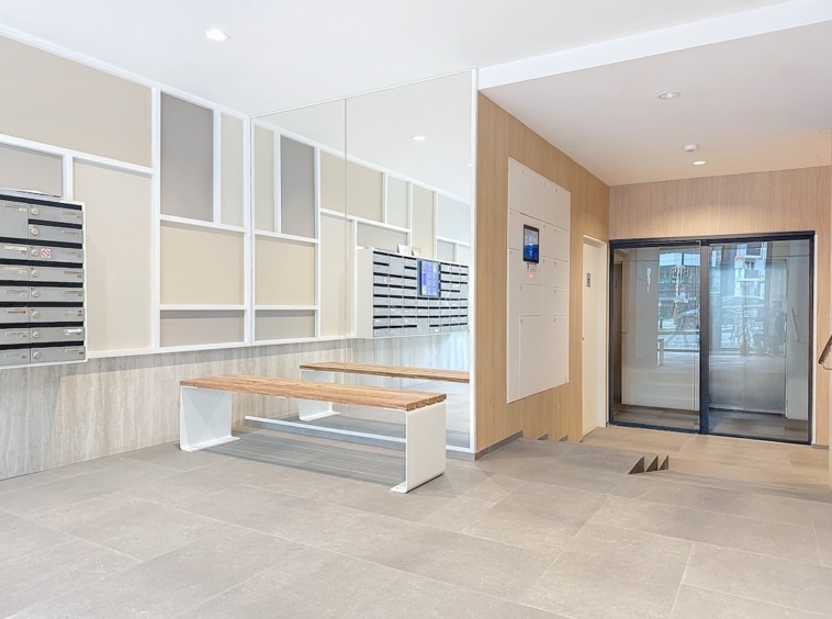 Hall d’entrée contemporain avec miroir, mailboxes élégantes, ascenseur en verre et mobilier minimaliste.