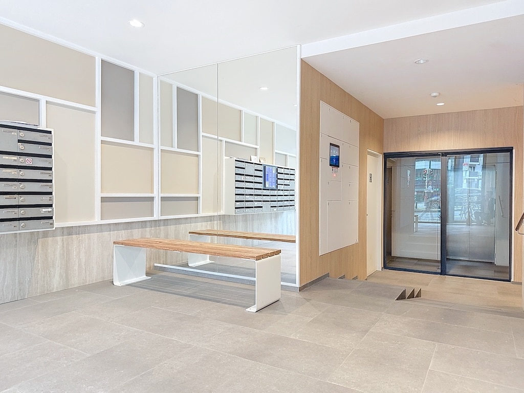Hall d’entrée contemporain avec miroir, mailboxes élégantes, ascenseur en verre et mobilier minimaliste.