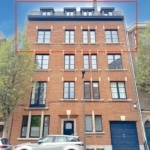 Immeuble urbain en brique rouge avec fenêtres noires, garage bleu et arbres verts.