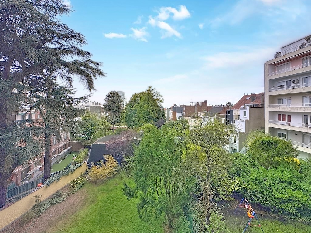 Parc urbain verdoyant avec terrains de jeux, bâtiments variés et ciel bleu clair.