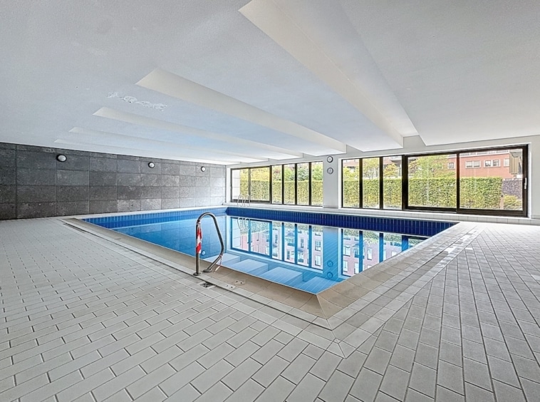 Piscine intérieure moderne avec lumière naturelle, design épuré et vue verdoyante apaisante.