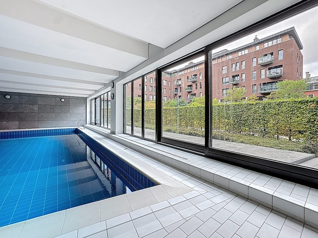 Piscine intérieure moderne avec vue sur jardin verdoyant et architecture résidentielle contemporaine.