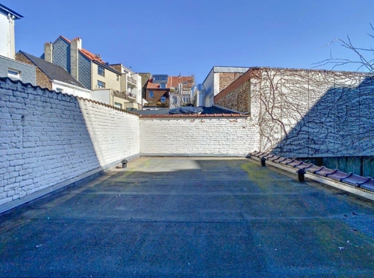 Terrasse urbaine paisible avec murs en brique, végétation, vue sur bâtiments sous soleil.