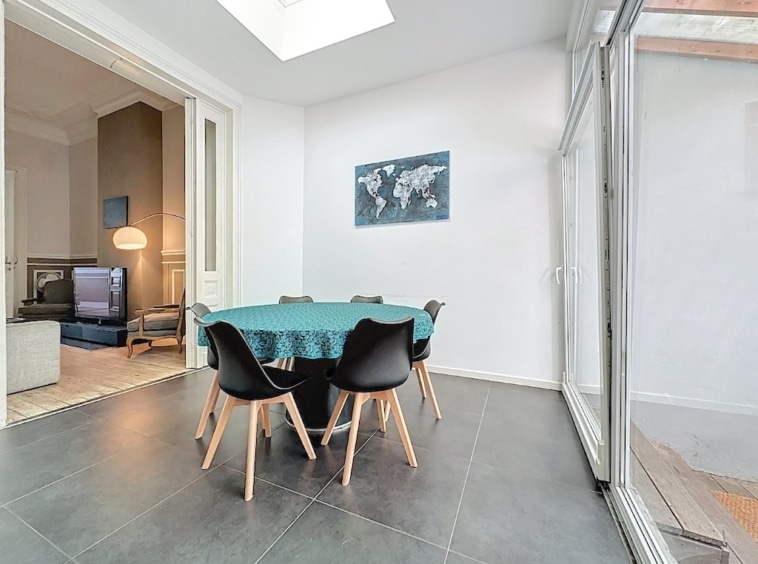 Salle à manger moderne lumineuse avec table colorée, chaises noires, fresque du monde, accès extérieur