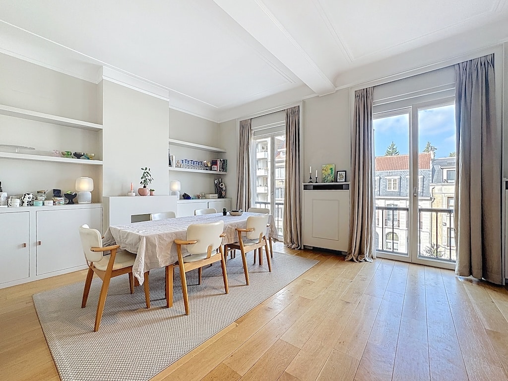 Salle à manger moderne lumineuse avec balcon, mobilier en bois clair, plantes et décoration élégante.