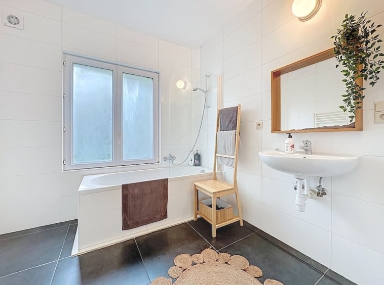 Salle de bain moderne avec baignoire, douche, miroir en bois et ambiance élégante.