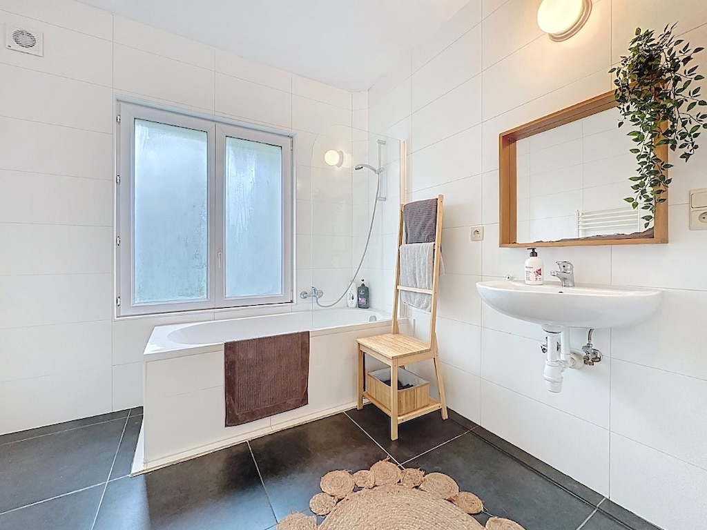 Salle de bain moderne avec baignoire, douche, miroir en bois et ambiance élégante.