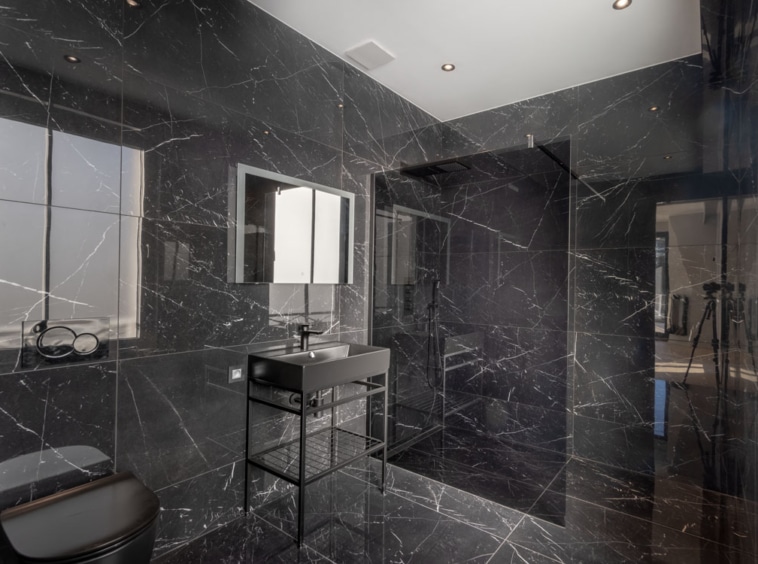 Salle de bain élégante en marbre noir moderne avec douche à l’italienne et miroir encadré.