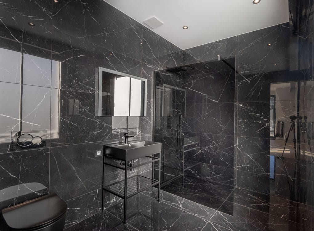 Salle de bain élégante en marbre noir moderne avec douche à l’italienne et miroir encadré.