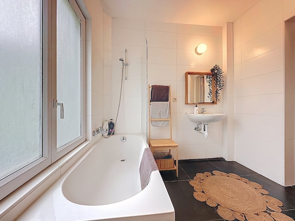 Salle de bain moderne minimaliste avec baignoire indépendante, douche, touches en bois et ambiance apaisante.
