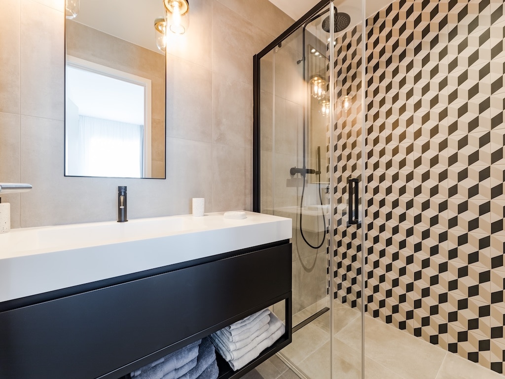 Salle de bain moderne, épurée, lumineuse avec mobilier minimaliste, douche en verre et éclairage chaleureux.
