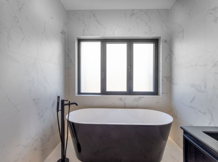 Salle de bain élégante avec baignoire noire, marbre clair et mobilier en bois sombre.